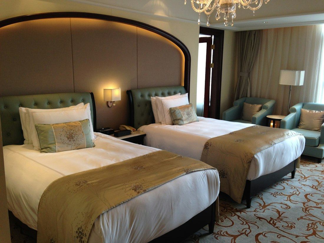 Habitación twin con dos camas, sillones verdes y alfombra estampada