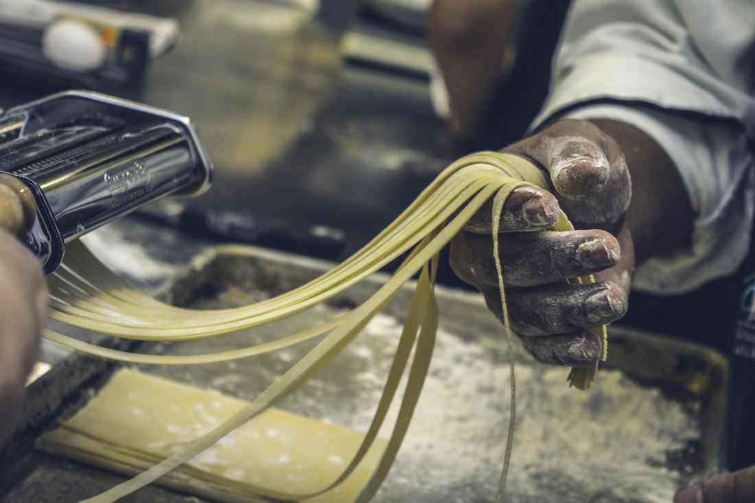 Manos del cocinero pasando masa fresca por la máquina de pasta