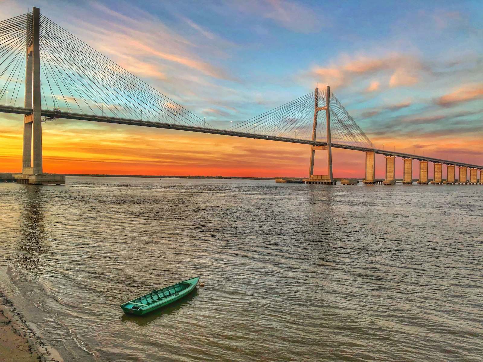 Puente atirantado sobre el río Paraná al atardecer, con una barca verde en la orilla