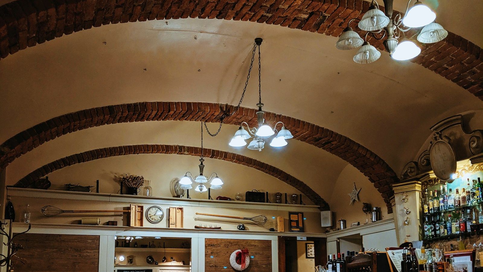 Salón con techo abovedado de ladrillo, mesas con mantel a cuadros y lámparas de araña
