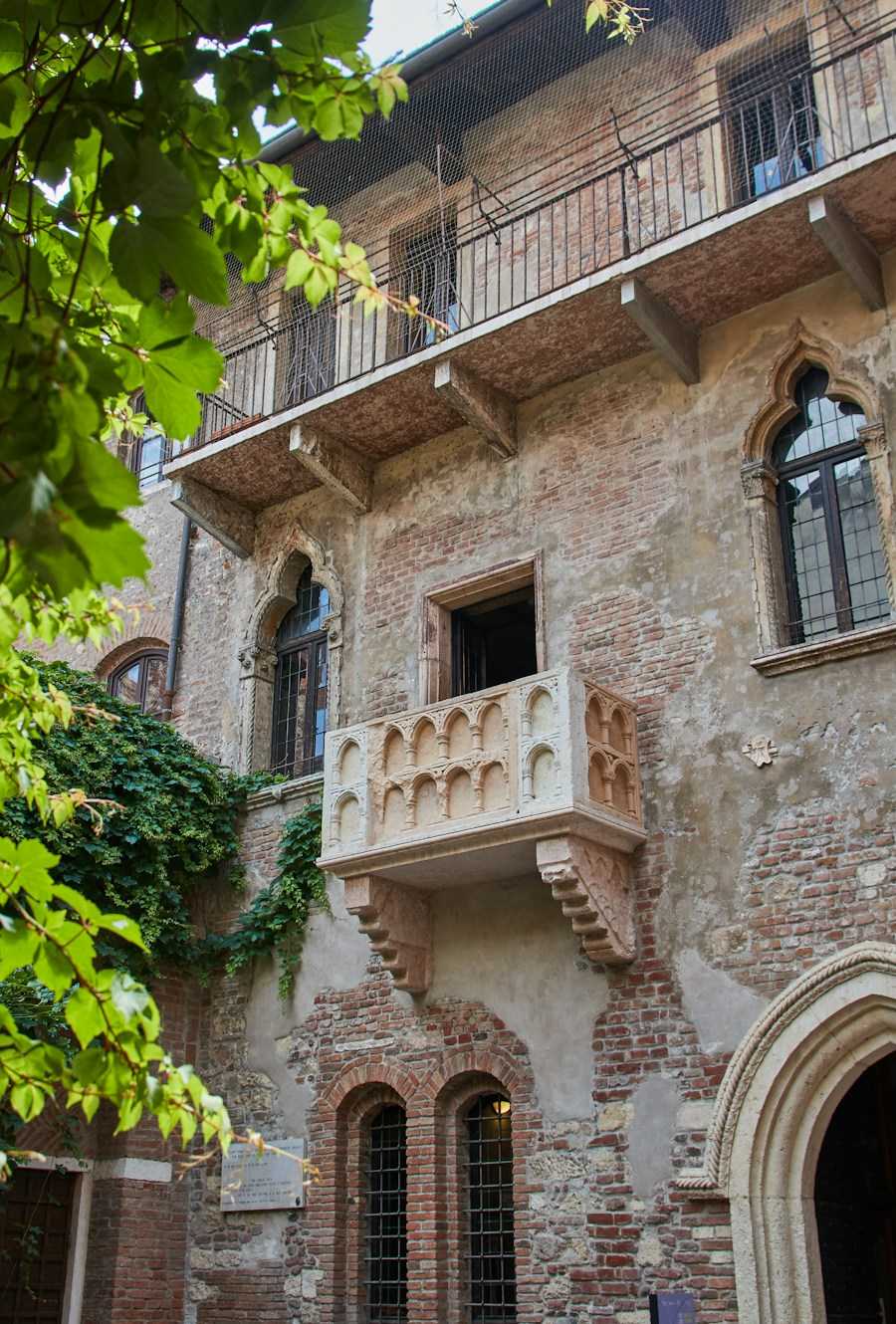 Balcón de piedra con ventanas góticas y hiedra en una casa antigua de Verona