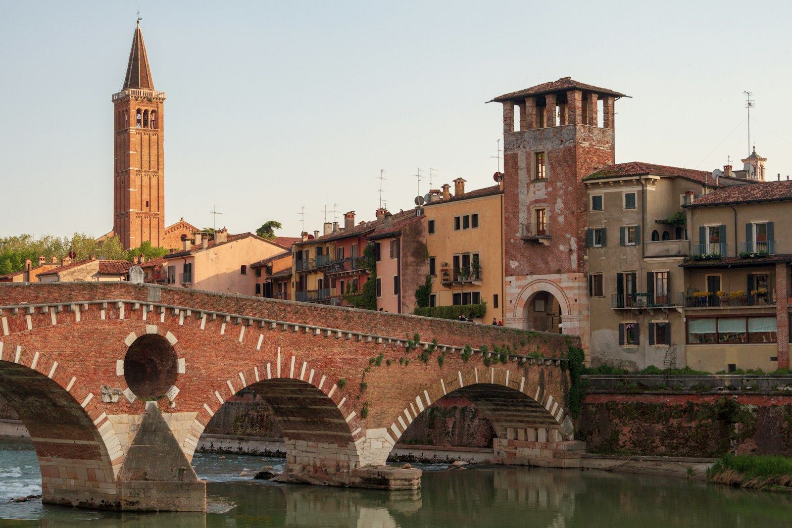Puente de piedra y ladrillo sobre el río en Verona, con torres al fondo